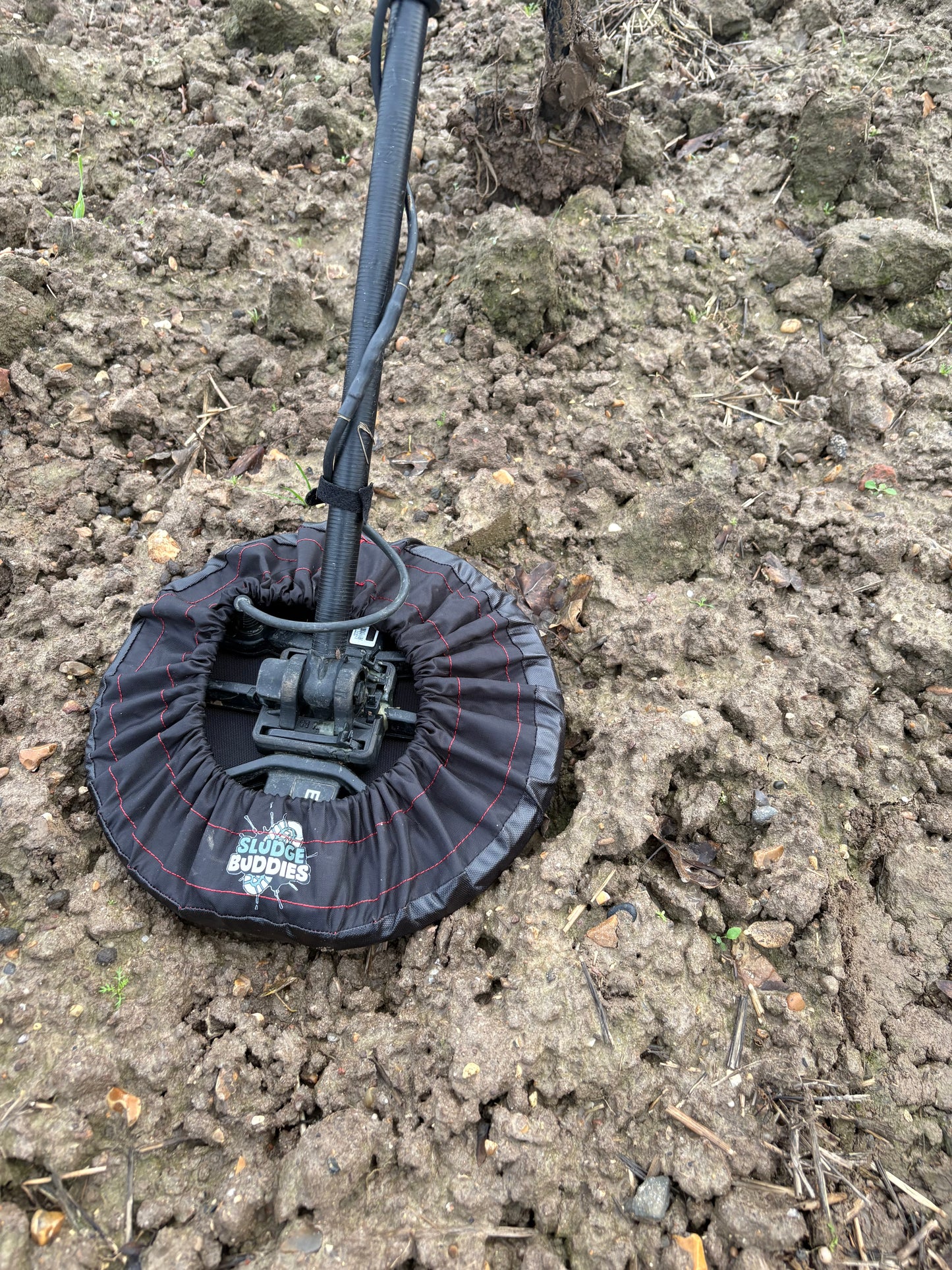 Sludge Buddies 11-inch coil cover fitted on a metal detector during field testing in muddy conditions.