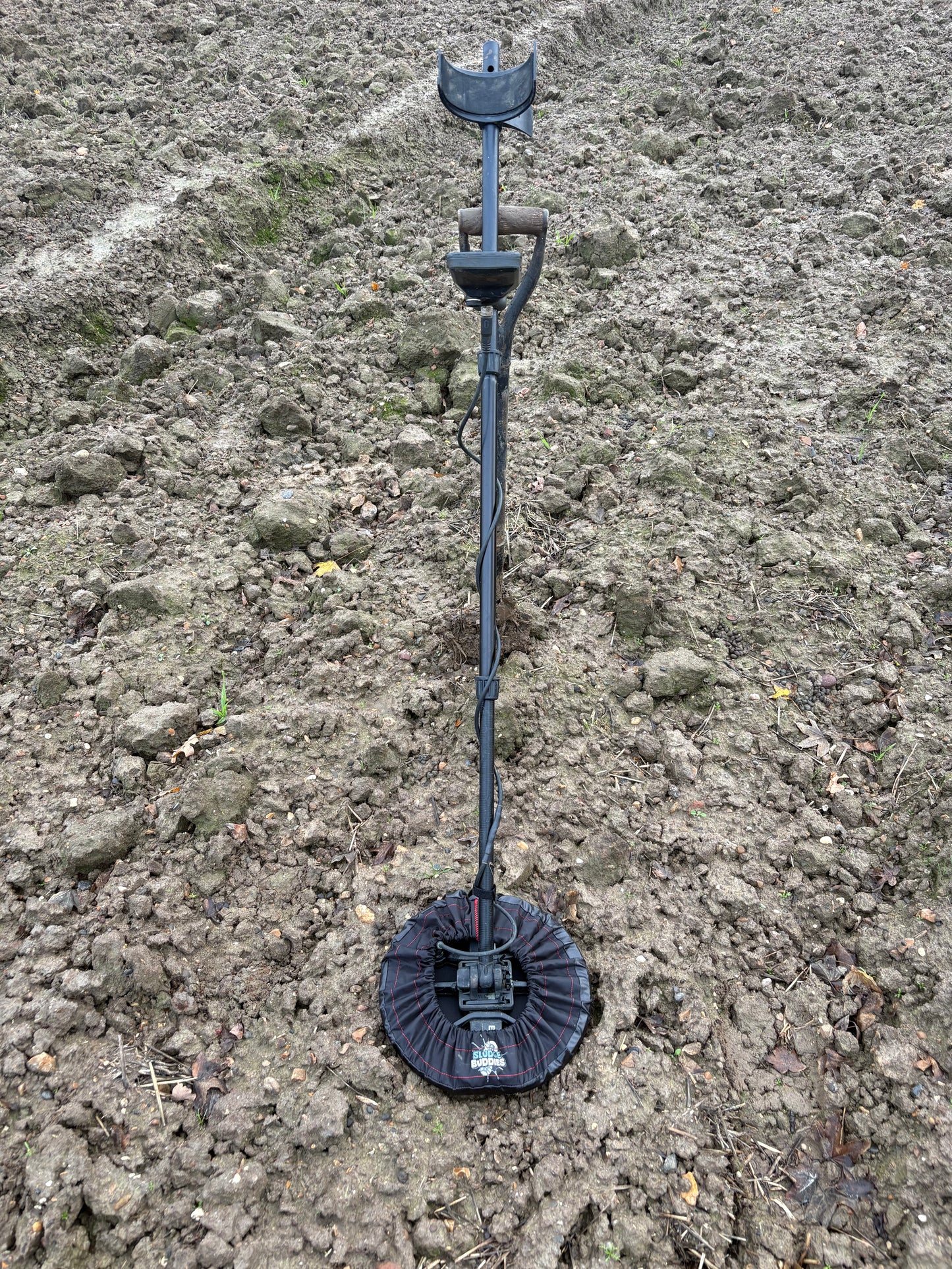 Sludge Buddies 11-inch coil cover fitted on a metal detector during field testing in muddy conditions.