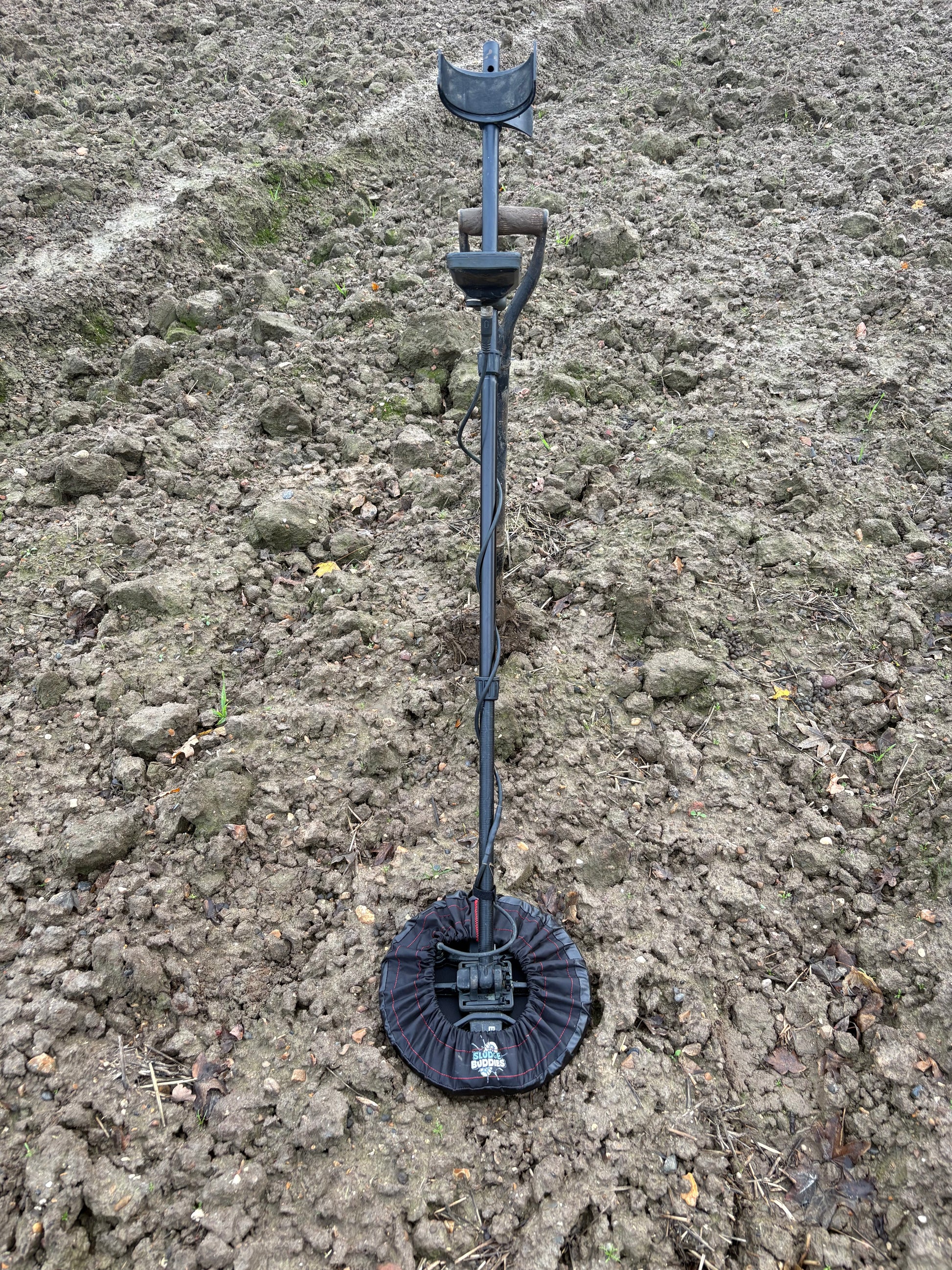 Sludge Buddies 11-inch coil cover fitted on a metal detector during field testing in muddy conditions.